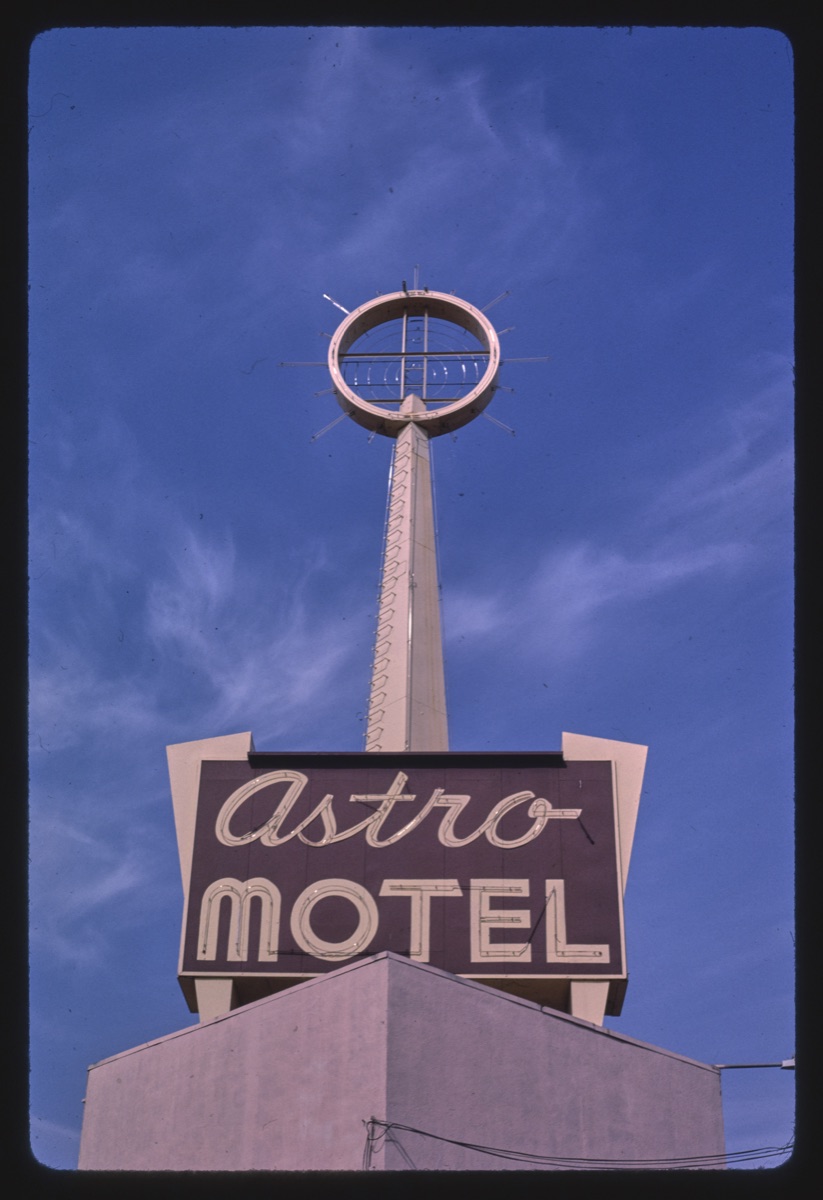 The Astro Motel sign: a tall mid-century pylon with a ringed starburst crown against a deep blue sky.